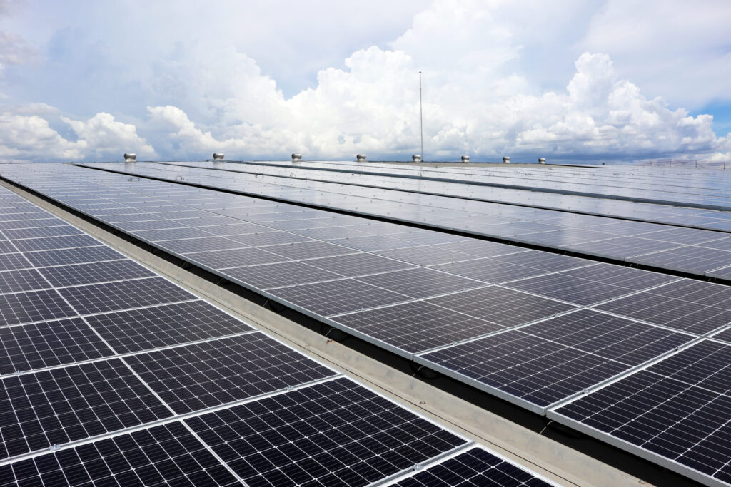 A large group of solar panels on the roof of an industrial building with blue cloudy sky.