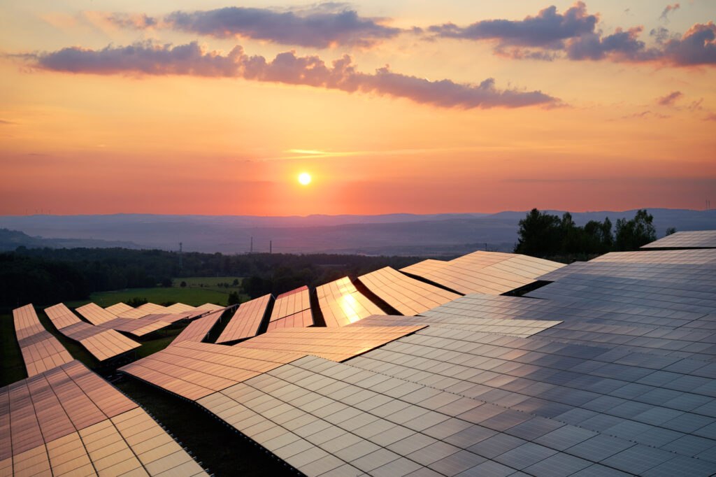 The sun setting over a field of solar arrays in a lush, green landscape.